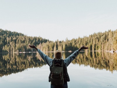 Woman raising arms in front of lake surrounded by arms